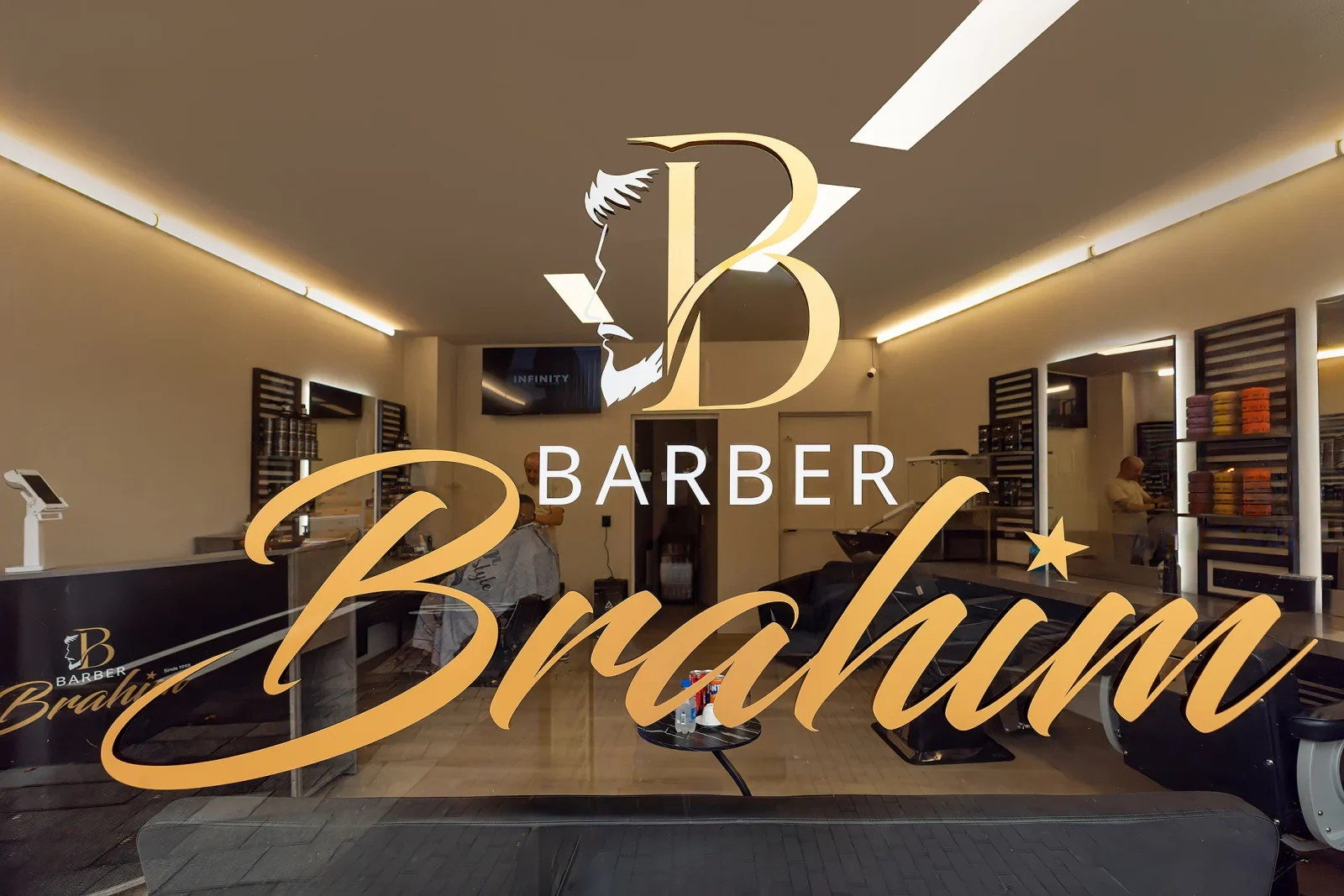 Het logo van Barber Brahim op de ruit, met zicht op de zaak