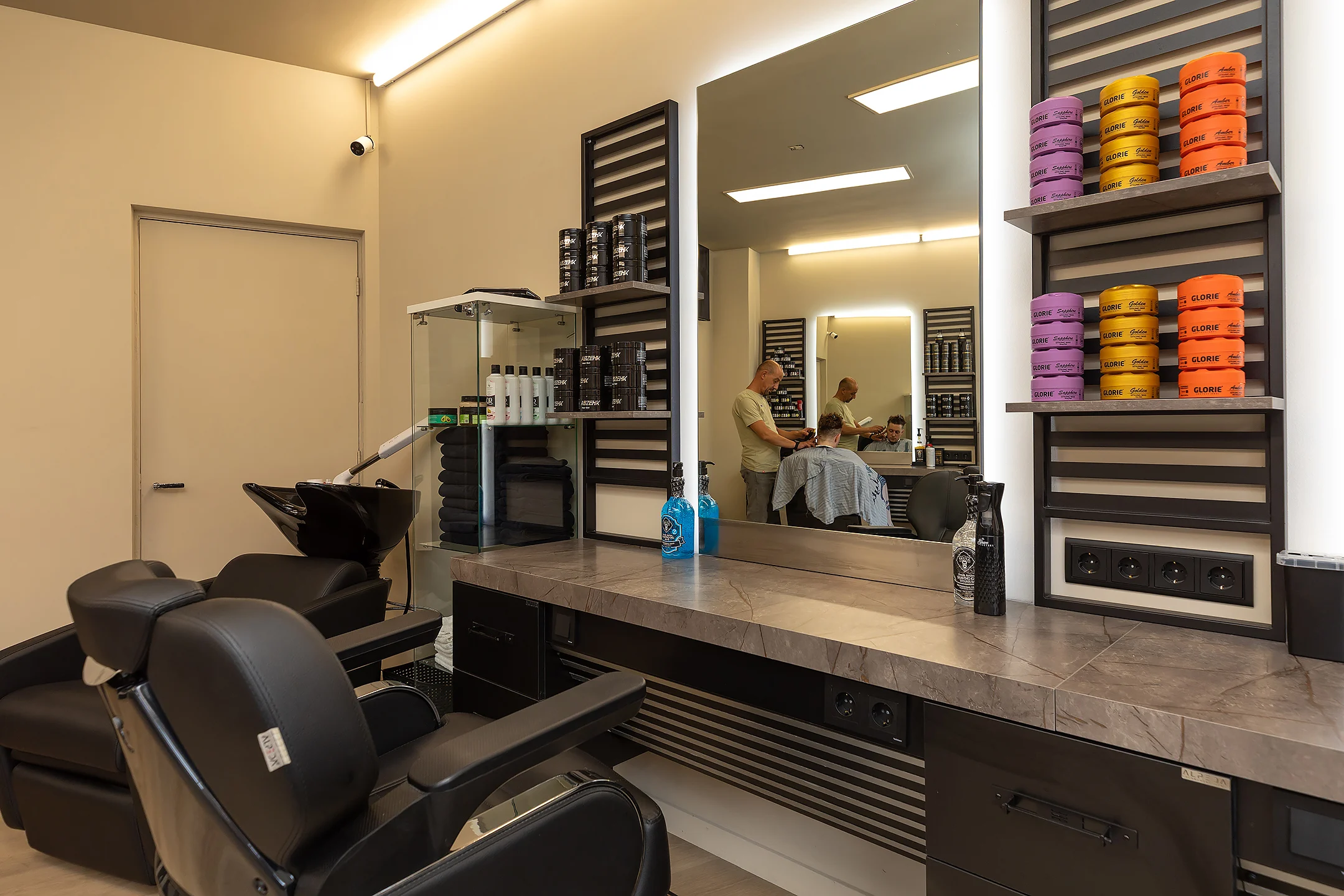 Haarproducten op de kaptafel, met een barbier aan het werk op de achtergrond